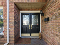 Old black double front doors with half-glass panels on a brick porch in Aurora before replacement.