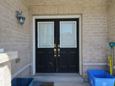 Old black double entry doors with glass panels on a brick porch before a modern Fiberglass Door Ajax replacement.