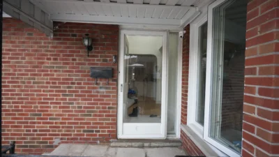 Old standard white storm door on a classic brick porch at Beacham Crest before a modern fiberglass replacement.