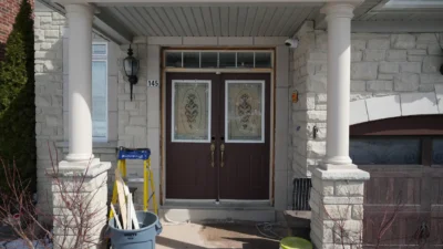 Old brown double entry doors with decorative glass inserts on a stone porch in Markham before replacement.