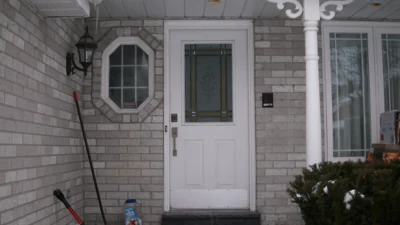 Old standard white front door on a snowy porch at Chambery Crescent before a custom replacement.