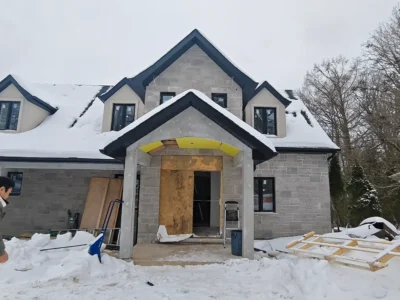 A boarded-up front entrance of a custom stone home under construction in Newmarket during a snowy winter, before fiberglass door installation.