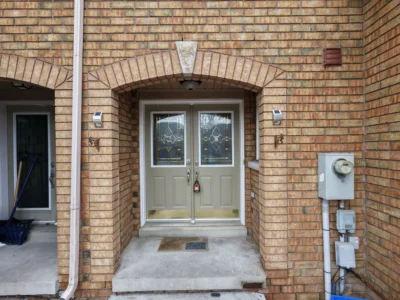 Old light-colored double entry doors with decorative glass inserts on a brick porch in Richmond Hill before replacement.
