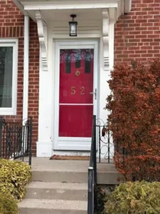 Old red front door with a white storm door on a downtown townhouse porch before replacement.